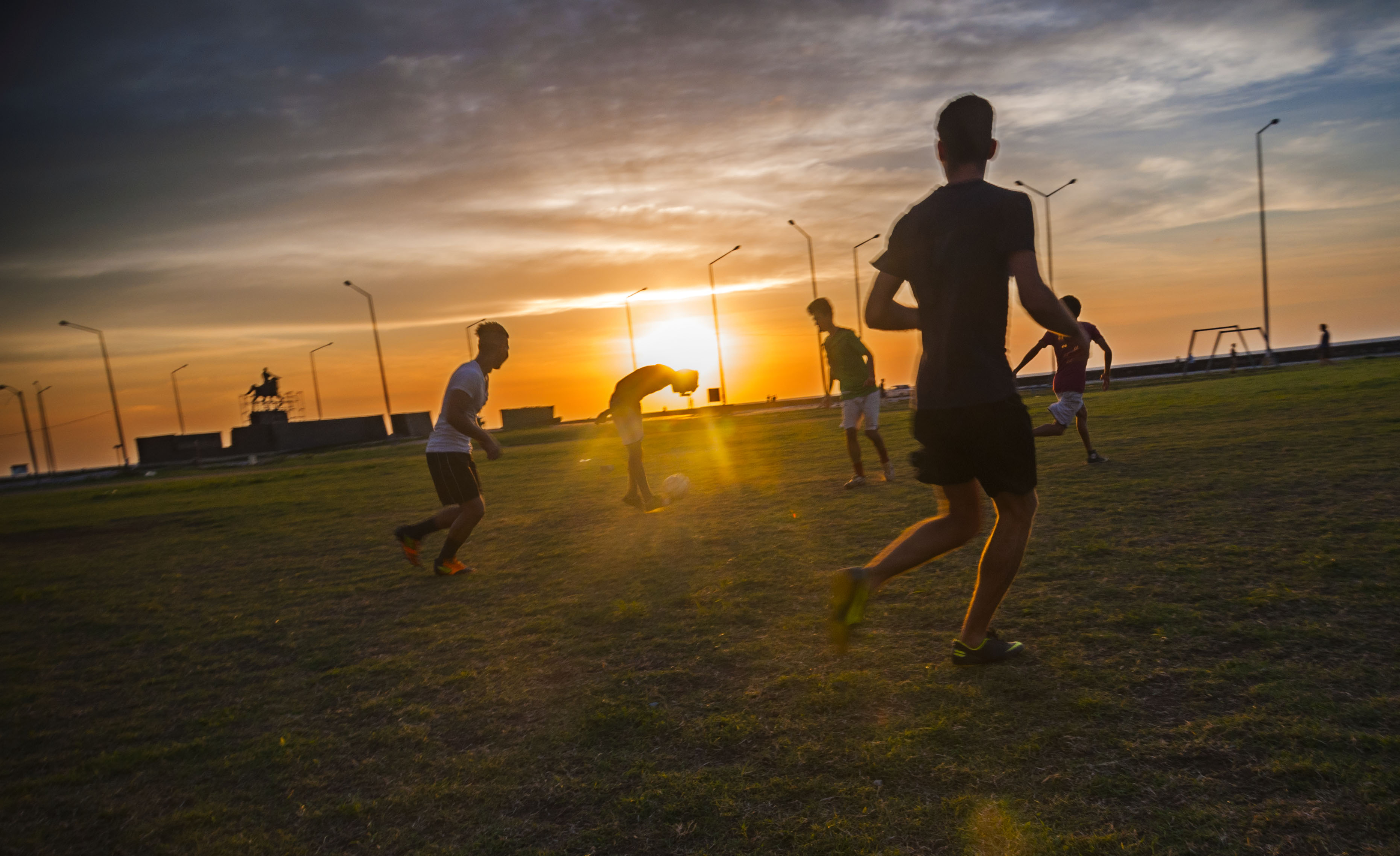 Group of young men playing soccer at sunset.